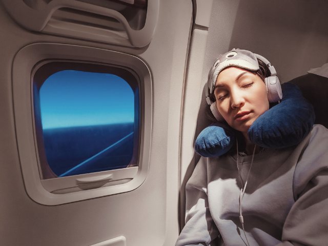 person resting their head near an airplane window while they sleep