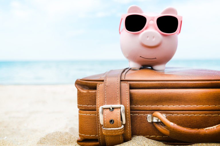 Pink piggy savings bank on a suitcase on the beach.