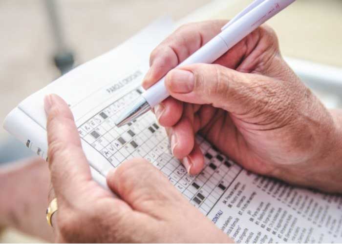 person holding pen working on a crossword puzzle