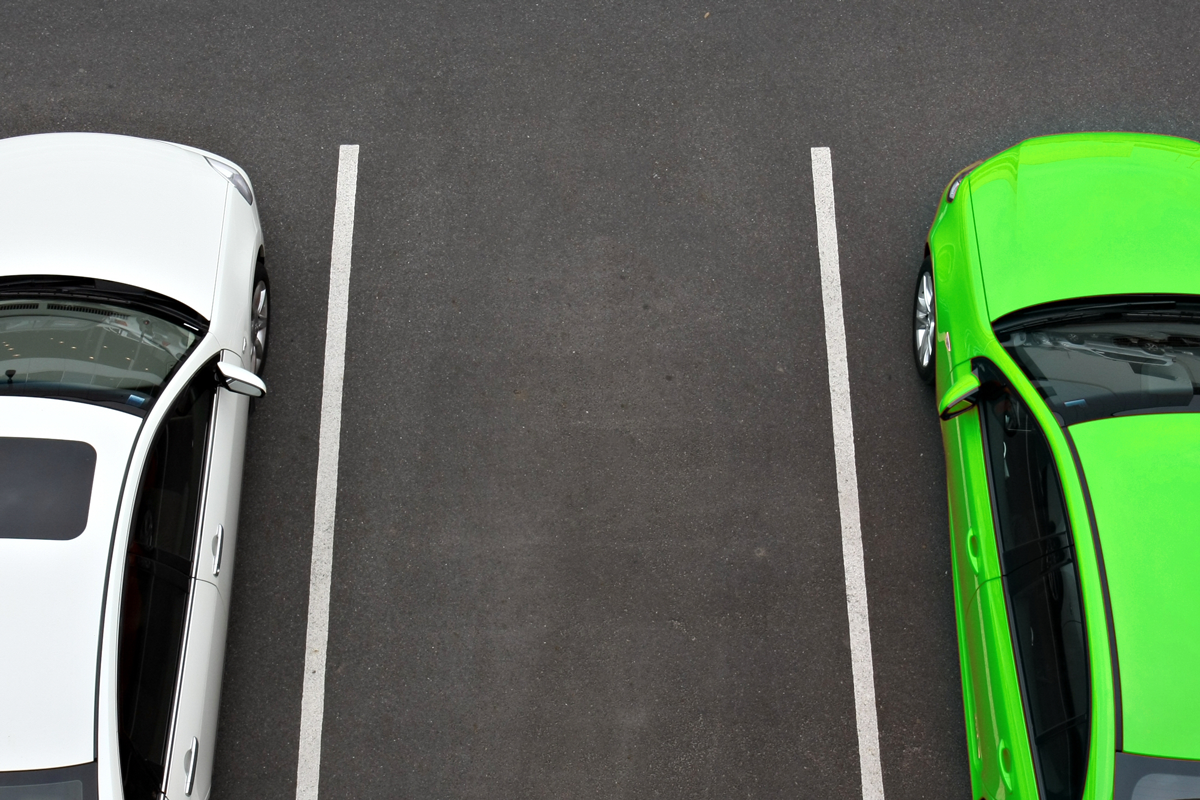 A white car and a green car parked at offsite airport parking facility.