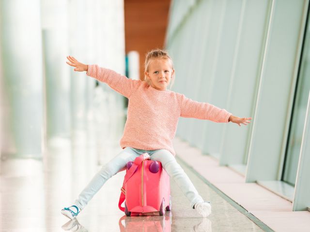 Young girl sitting on a pink suitcase at the airport.