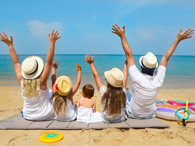 Family sitting at the beach looking at the ocean with their arms raised in the air.