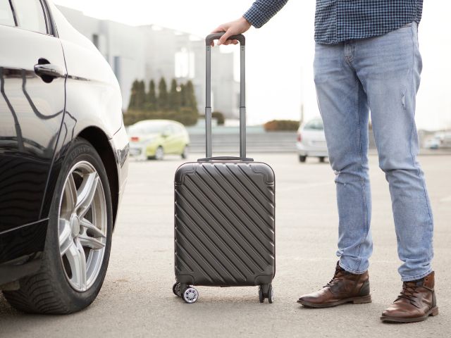 man standing next to his car with a roller bag in his hand